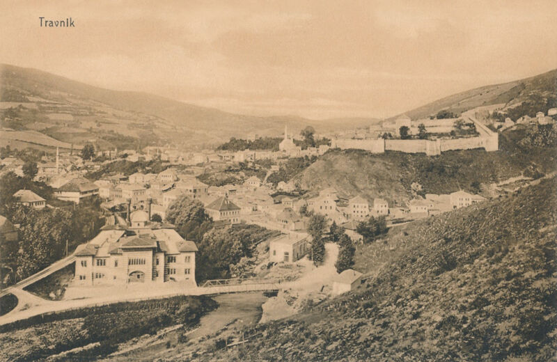 A wide vintage postcard view of the town of Travnik featuring the fortress and surrounding valley.