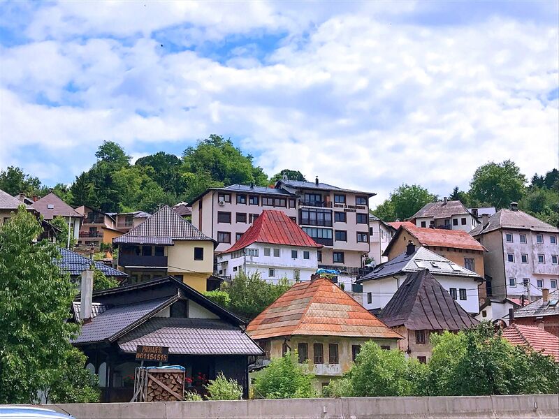 A view of hillside traditional houses in Travnik set against green foliage.
