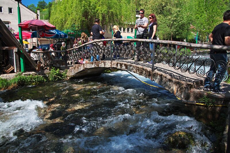 Visitors stand on a stone bridge spanning the Plava Voda spring in Travnik.
