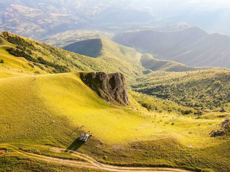 Off-road vehicles rest on the grassy slopes of Mount Vlasic overlooking surrounding valleys.